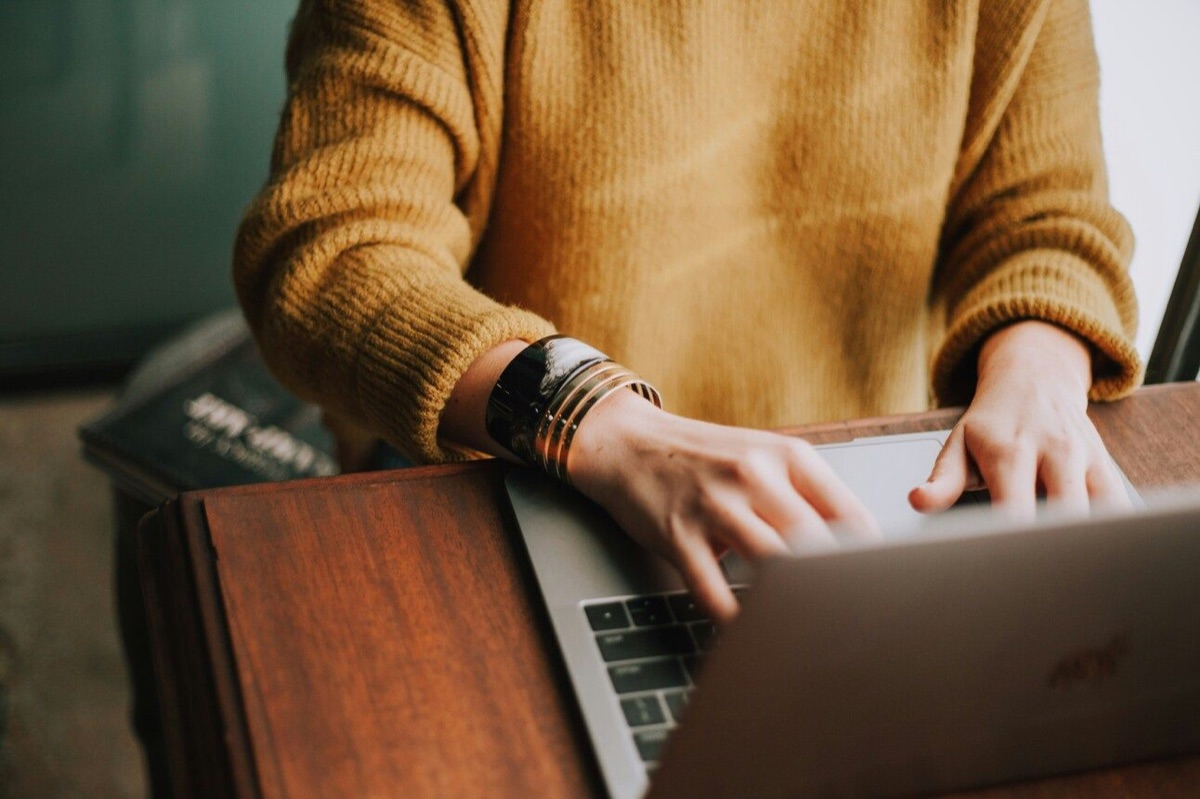 A person in a mustard sweater typing on a laptop